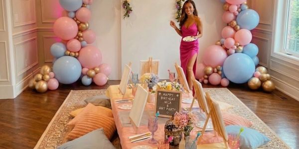 Birthday art party setup with colorful balloons and a woman in a magenta dress.