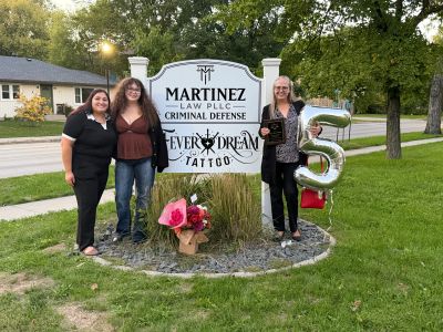Three women standing by a sign with flowers and balloons.