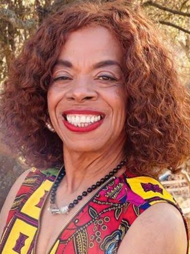 Smiling woman with curly hair in a colorful patterned dress.