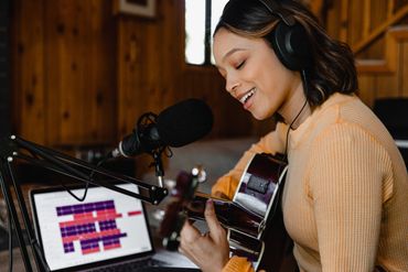 Woman playing guitar and singing while recording with microphone and headphones and daw