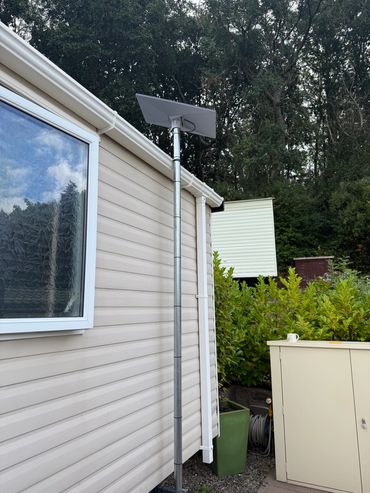 A solar panel mounted on a tall pole beside a beige house exterior.