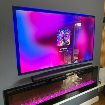 TV displaying colorful album art with a soundbar and electric fireplace below.