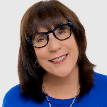 Smiling woman with glasses and brown hair wearing a blue top.