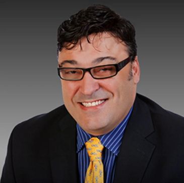 Smiling man in glasses wearing a suit and patterned yellow tie.