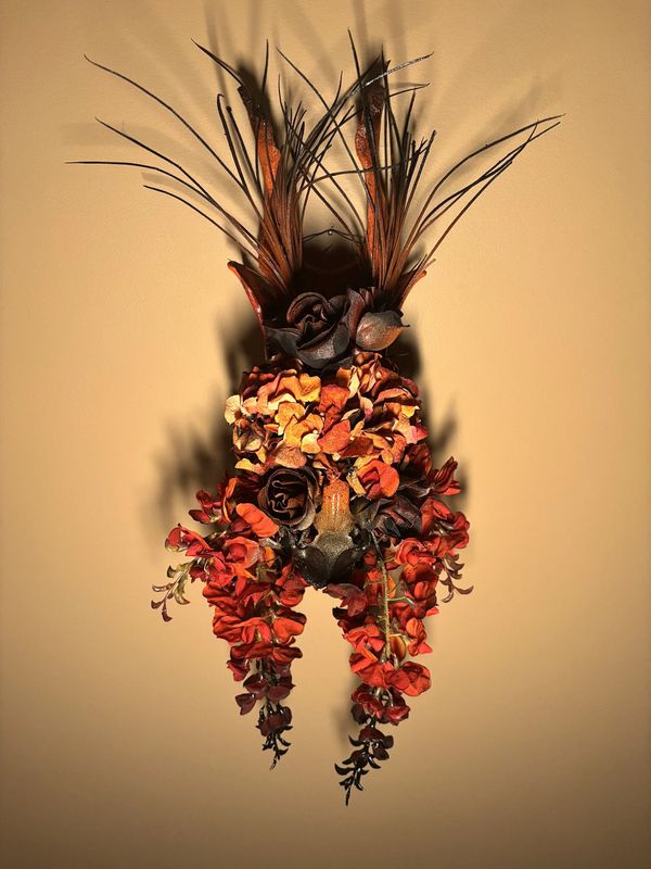 Decorative flower arrangement with dark and orange blooms on a beige wall.