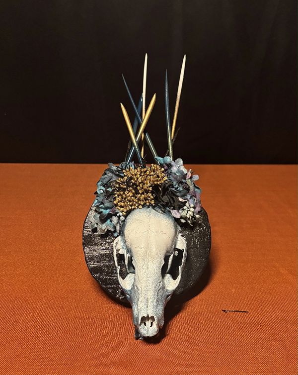 Decorative animal skull with flowers and sticks on a black base.