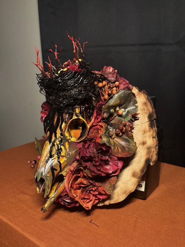 Decorative skull with flowers and a nest on a wooden base.