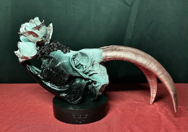 Colorfully painted animal skull with large curved horns on a black circular base.