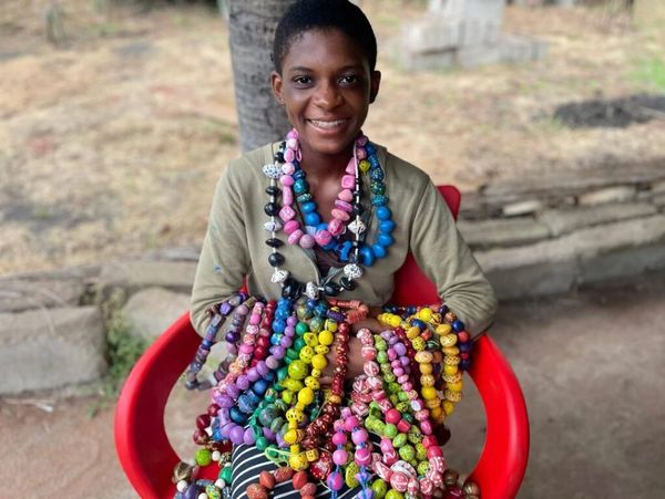 Smiling person wearing colorful beaded jewelry, sitting on a red chair.