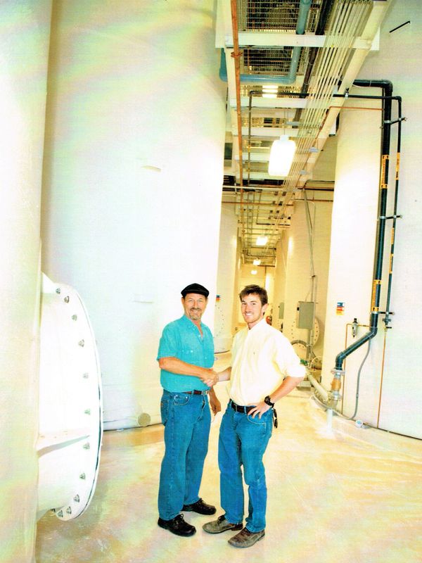 Two men shaking hands in an industrial setting with large tanks.