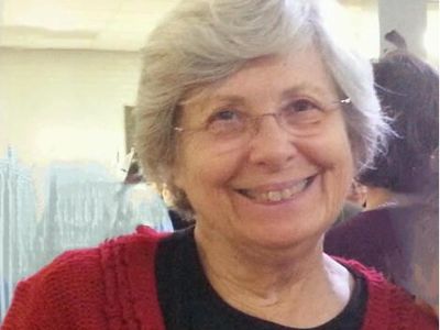 Smiling elderly woman wearing glasses and a red sweater.