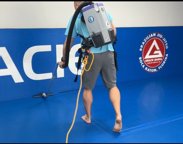 Person vacuuming blue mats in a Brazilian Jiu-Jitsu gym.