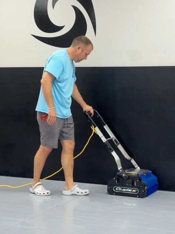 Man cleaning floor with a Duplex machine in a gym with black and white walls.