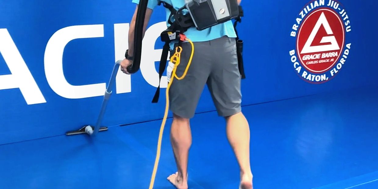Man using an industrial vacuum to clean blue Jiu Jitsu floor mats at Gracie Barra Boca Raton Florida