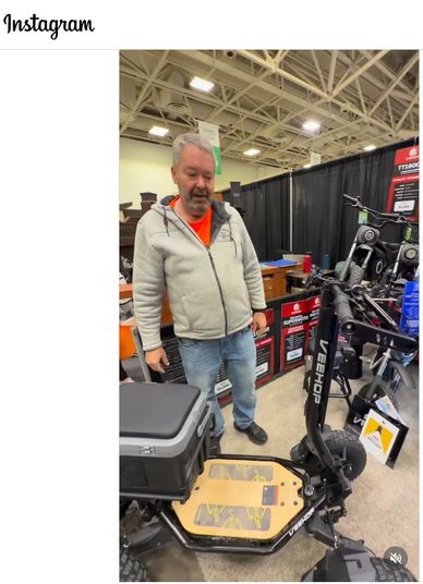 Man showcasing a large electric scooter at an indoor exhibition.