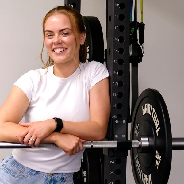 Smiling woman leaning on a barbell in a gym.