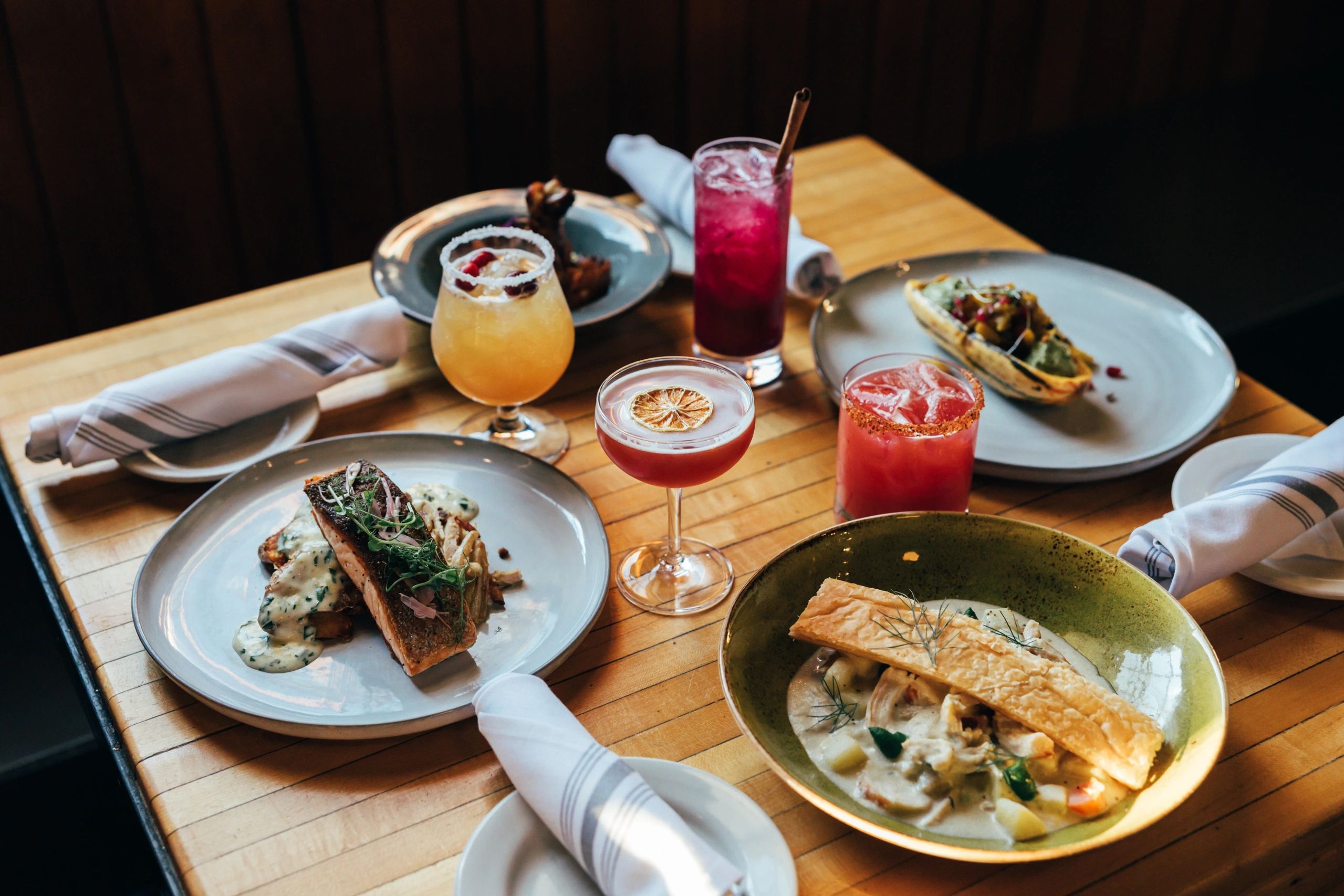 Table of food at Gather featuring Salmon and stew, along with drinks.
Photo Credit: Dawson Renaud