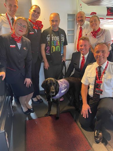 Group photograph of Cabin crew and pilots with Jon Fletcher and assistance dog Georgia a black Labra
