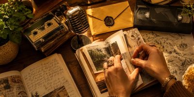 Hands arranging photos in a vintage scrapbook surrounded by nostalgic items.