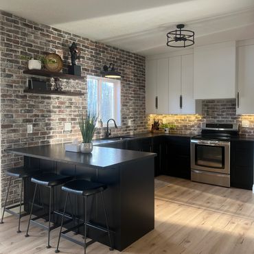 Modern kitchen with brick backsplash, black island and white cabinets in Grande Prairie.