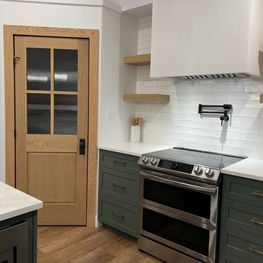 Green shaker cabinets with white subway tile backsplash and wood pantry door in Grande Prairie.