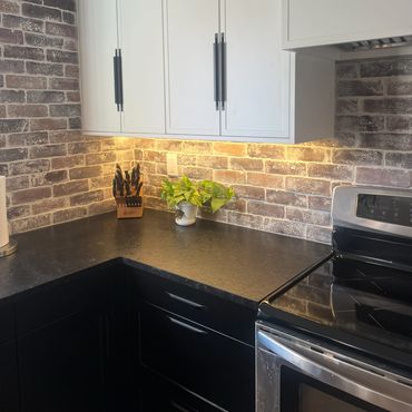 Kitchen with brick backsplash, black shaker cabinets and white slim shaker uppers in Grande Prairie.