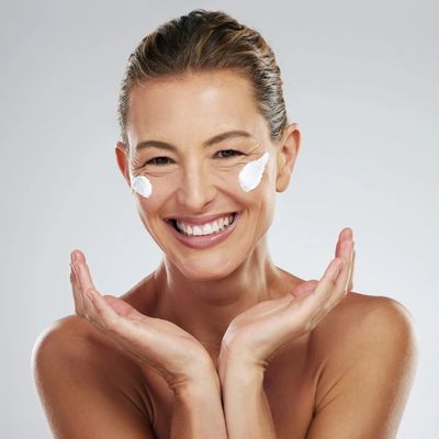 Smiling woman with cream on cheeks, showing fresh skincare routine.