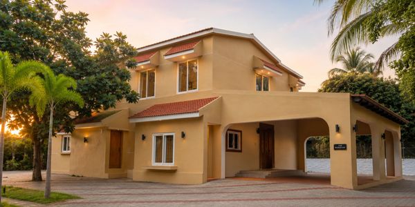 Modern two-story beige house with a red tile roof and a spacious driveway surrounded by greenery.
