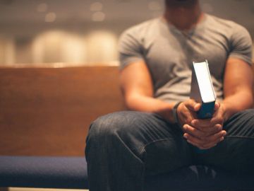 A man sitting on a bench holding a closed book with both hands.