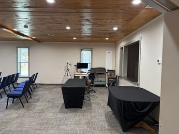 A clean conference room with rows of chairs, covered tables, and a computer setup.
