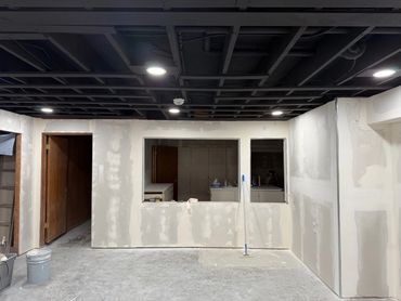 Room under renovation with drywall and black ceiling grid.