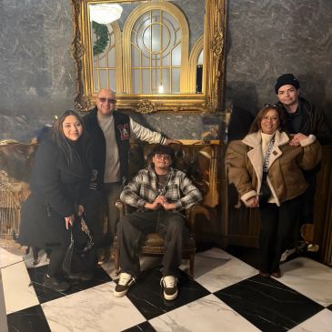 Group of five people posing indoors on a checkered floor.
