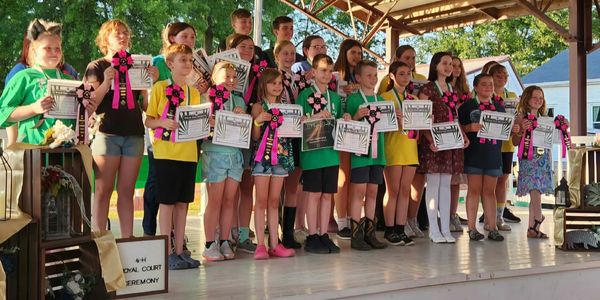 Children proudly display certificates and ribbons at an award ceremony on a stage.