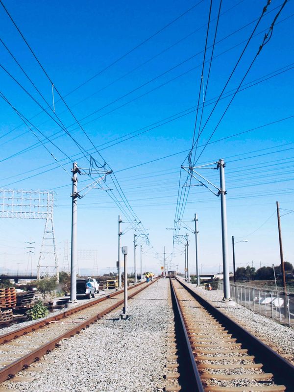 Railway tracks with power lines against a clear blue sky.