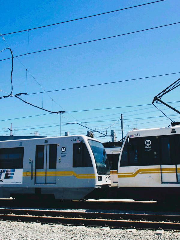 Two white metro trains face each other on tracks under a clear blue sky.