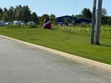 Small red and white lighthouse on a grassy hill near a parking lot.