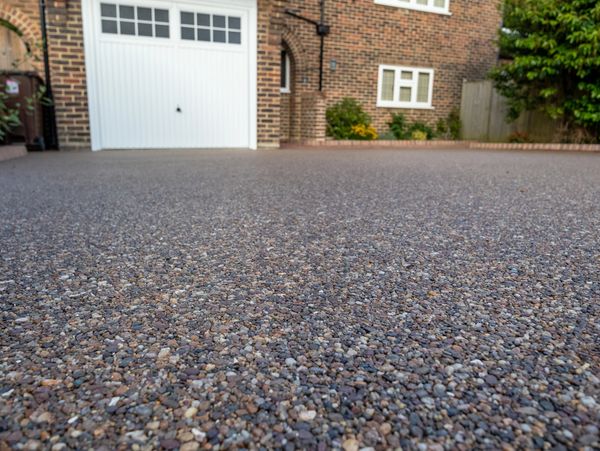 Close-up of a pebble driveway leading to a garage door of a brick house.