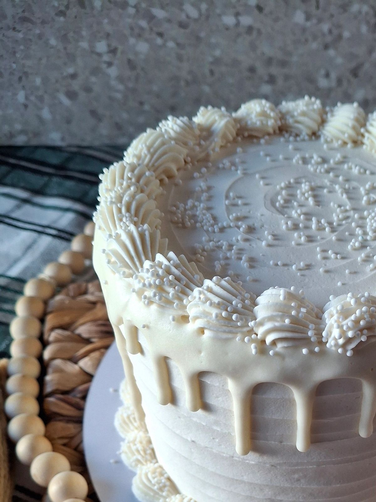 white buttercream cake with scalloped buttercream piping, white sprinkles, white drip along edge