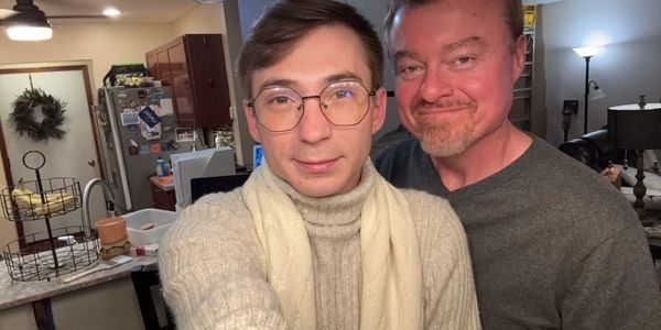 Two men smiling together in a cozy kitchen setting.