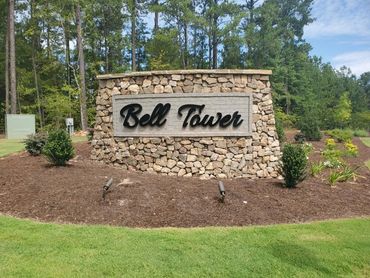 Stone sign reading 'Bell Tower' in a landscaped area with trees around.