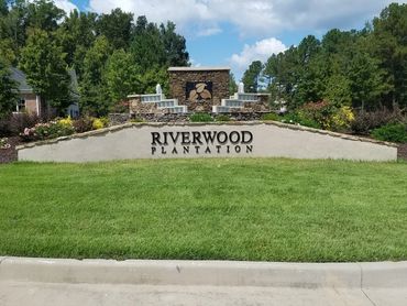 Entrance sign for Riverwood Plantation community with green lawn and clear sky.