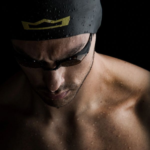 Focused swimmer in cap and goggles, water droplets on skin.