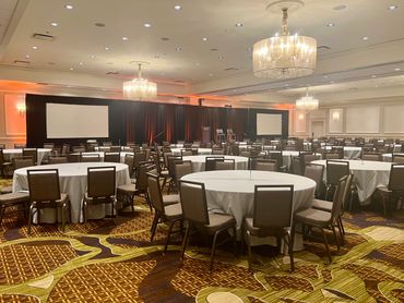 Spacious conference room with round tables, chairs, and large projection screens.