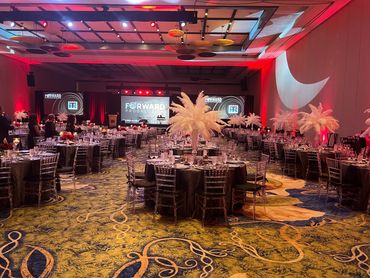 Elegant banquet hall set for a formal event with feather centerpieces and ambient red lighting.