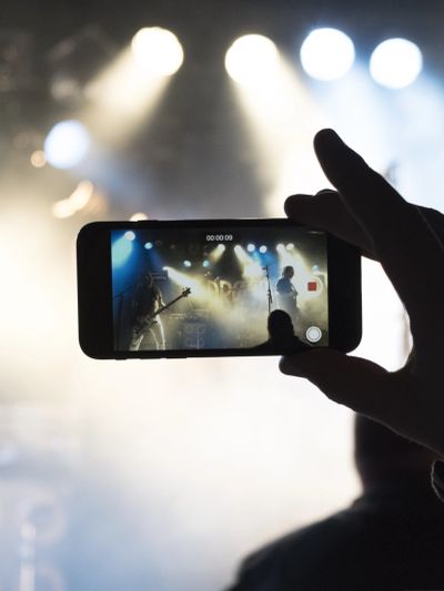 A person recording a live concert with a smartphone in low light.