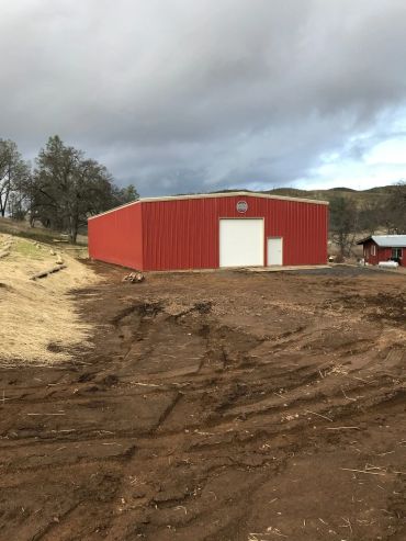 Red barn with white doors on muddy land under a cloudy sky.