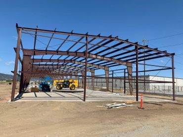 Steel frame structure under construction on a dirt lot.