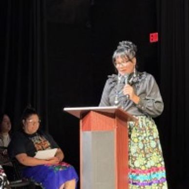 A woman speaking at a podium in traditional attire on stage.