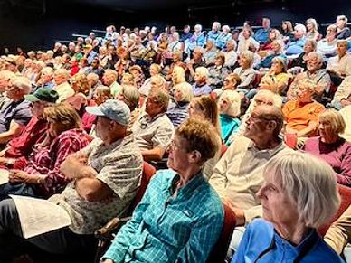 A large audience of older adults attentively watching a presentation.