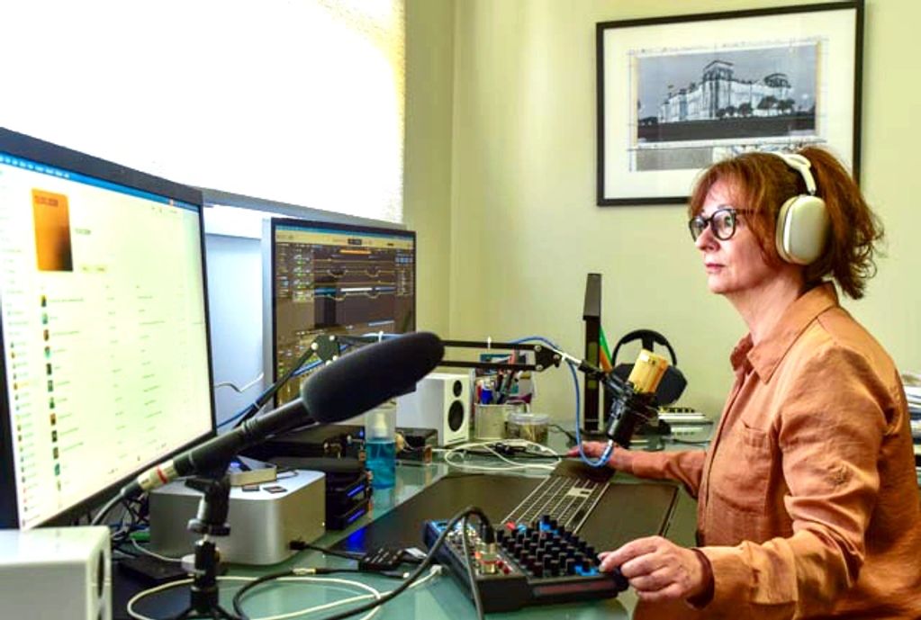 A woman with headphones working at a dual-monitor audio editing setup.